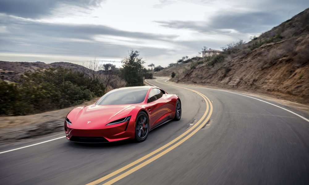A red Tesla Roadster driving around a turn